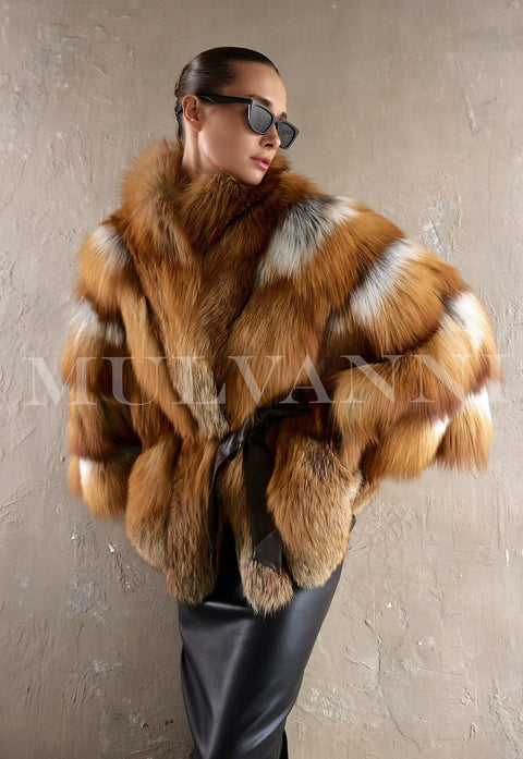 Woman confidently models an opulent red fox fur coat with an exaggerated silhouette and rich natural tones, styled with a black leather belt that defines the waist and enhances the coat’s statement appeal.