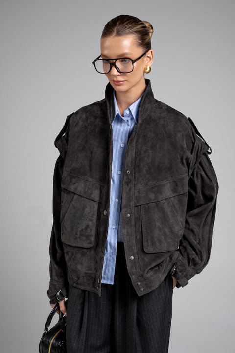 A woman wears a charcoal suede jacket crafted from soft, high-quality suede leather, featuring a flattering fit and rich hue for versatile style.