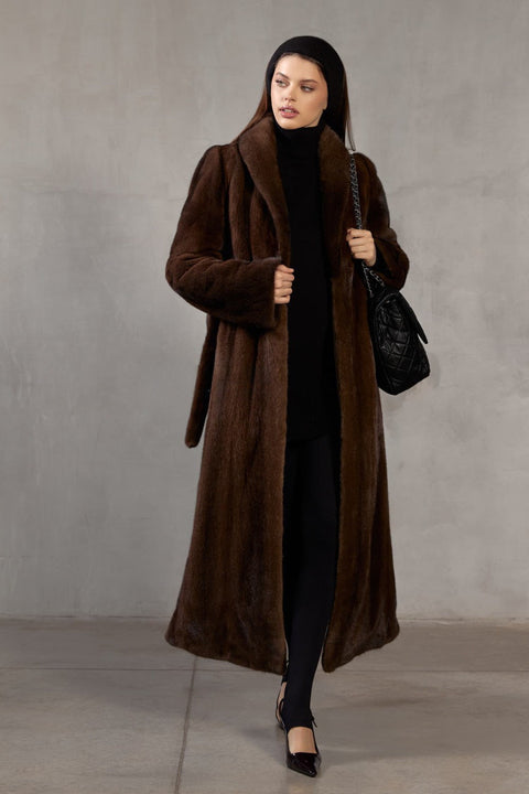 A woman stands elegantly in a floor-length dark brown mink coat, designed for both dramatic warmth and elevated style.