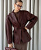 A woman wearing a burgundy leather blazer jacket with a cinched waist, crafted from soft, supple leather for a flattering, elegant silhouette perfect for work or refined casual looks.