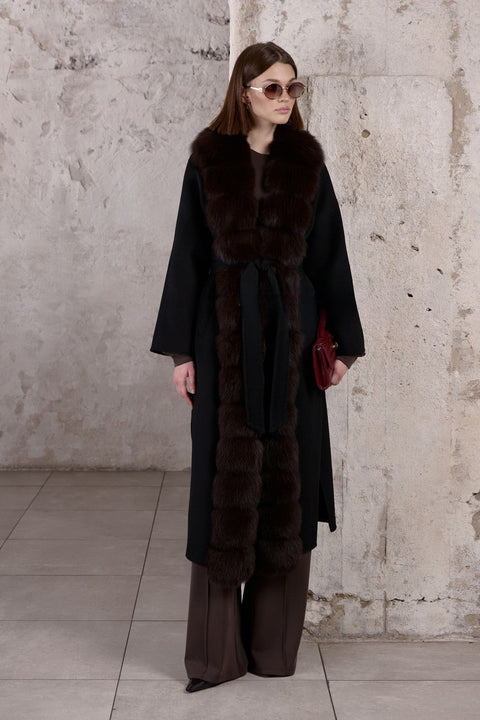 A woman wears a luxurious black cashmere coat, cinched at the waist with a belt and adorned with soft brown fox fur, creating a flawlessly elegant silhouette.